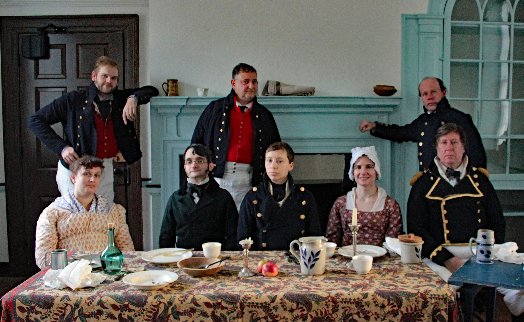A Ship's Company crew sits around a dinner table at a re-enactment