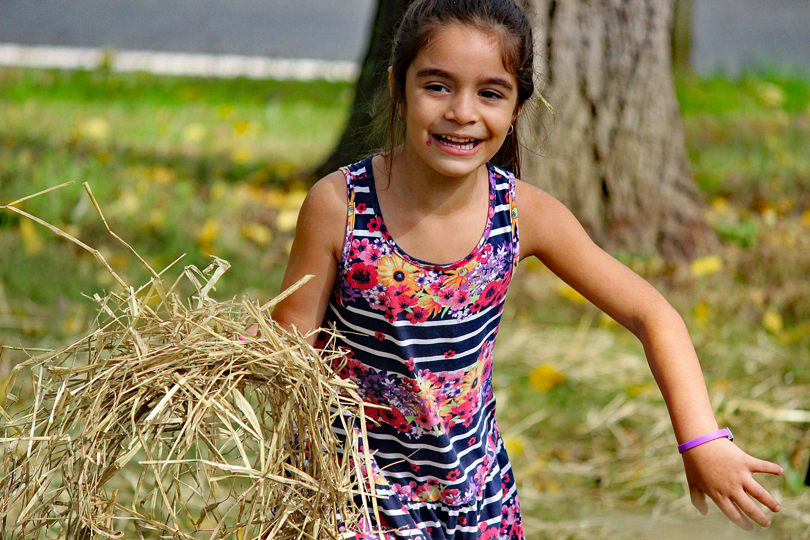 A young girl smiles as she gathers straw to stuff in a scarecrow