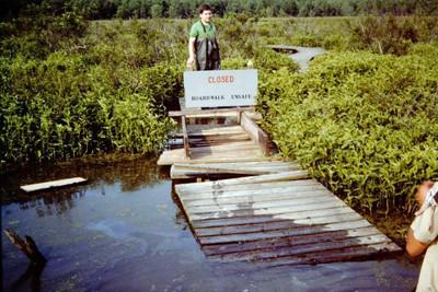 A closed sign stands next to a flooded, collapsed section of the boardwalk