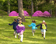Several GIrls Scouts running across a field toward their tents